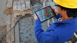 Bauarbeiter mit iPad, im Hintergrund eine Baustelle.