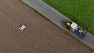 Aus der Vogelperspektive: Ein Roboter auf einem Feld, ein Weg, auf dem ein Traktor fährt.