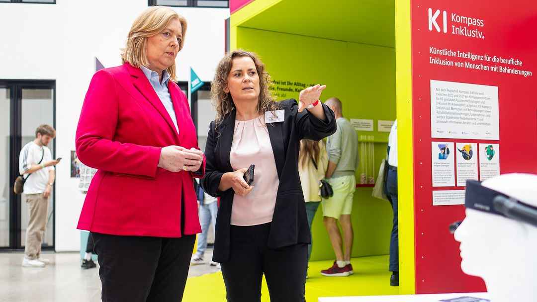 Susan Beudt, stellvertretende Leiterin des Educational Technology Lab am DFKI und Konsortialleiterin des Projekts KI-Kompass Inklusiv (r.) erläutert Bundesministerin Bärbel Bas (l.), wie KI-gestützte Assistenztechnologien Menschen mit Behinderungen im Arbeitsleben unterstützen können